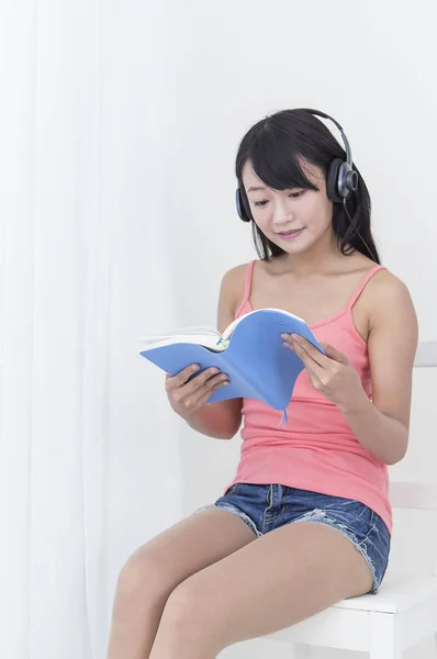 Jovem Usando Fone Ouvido Sorrindo Lendo Livro — Fotografia de Stock