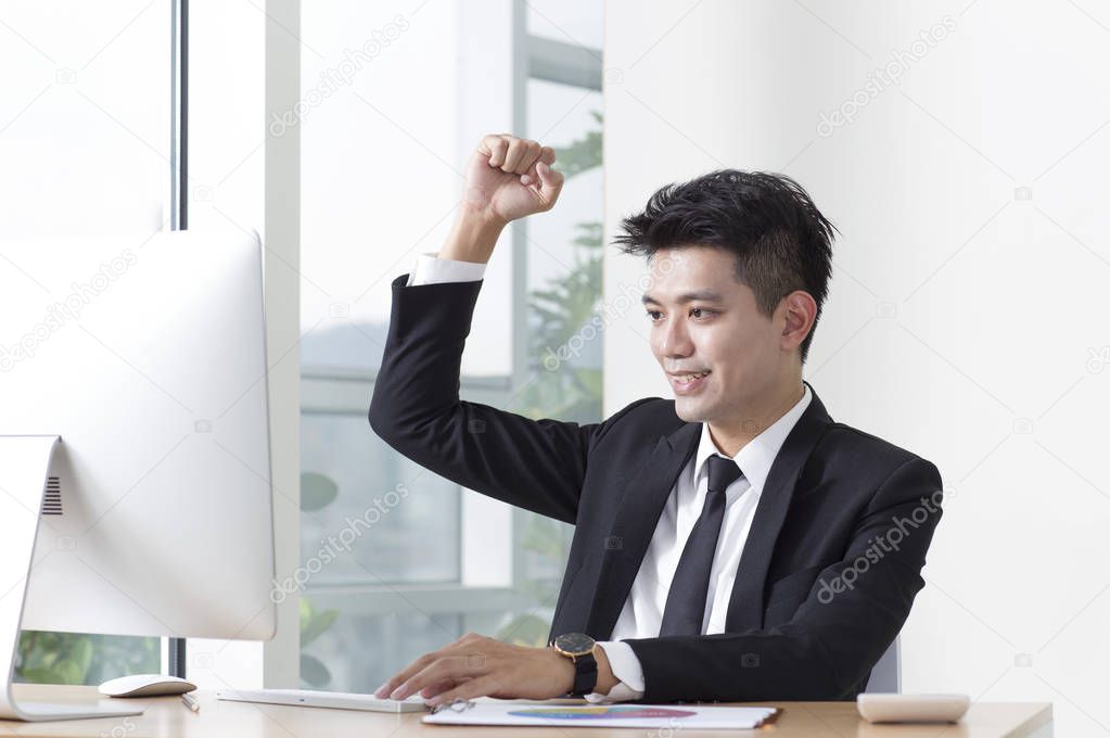 Young man in a suit sitting at the desk hands up and smiling