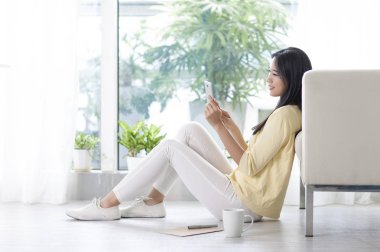 Kanepe onun smartphone kullanarak gülümseyen oturan genç kadın