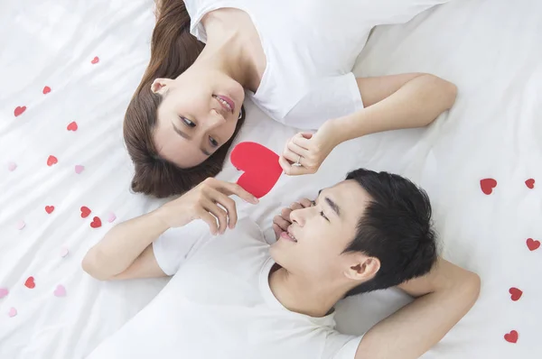 若いカップルの心を持って 笑顔のベッドの上に横たわる — ストック写真