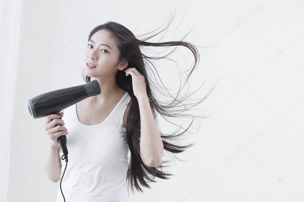 Young Asian woman drying her hair and smiling at the camera