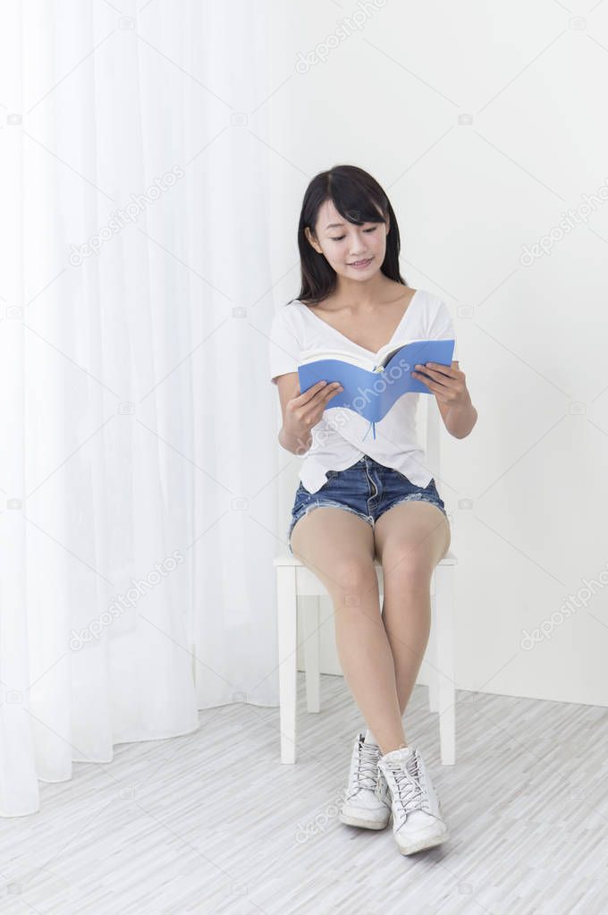 Young girl sitting on the chair and smiling reading a book