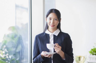 Bir fincan kahve tutarak ve kameraya gülümseyen Genç Asyalı kadın
