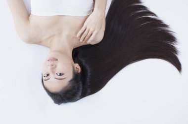 Siyah uzun saçlı yalan ve kameraya gülümseyen Genç Asyalı kadın