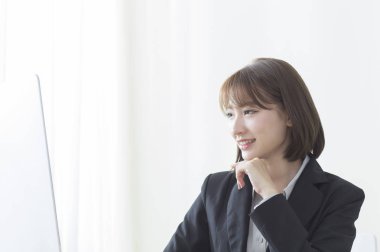 Bilgisayarı kullanan gülümseyen bir takım elbise giyen genç Asyalı kadın