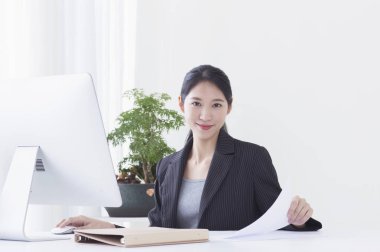 Bilgisayarını kullanarak ve kameraya gülümseyen oturan genç Asyalı kadın