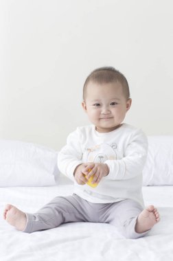 Oyuncakla oynamak yatağın üstüne oturan genç Asya bebek