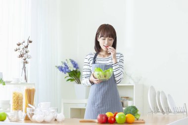 Genç Asyalı kadın mutfakta salata yemek