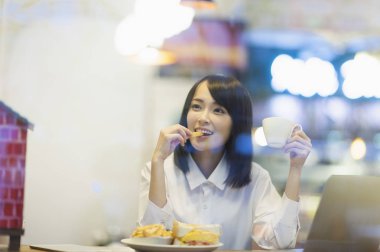 Abur cubur yeme ve kameraya gülümseyen bir takım elbise giymiş genç Asyalı kadın