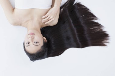 Genç Asyalı kadın siyah uzun saçlı yalan ve kameraya bakıyor