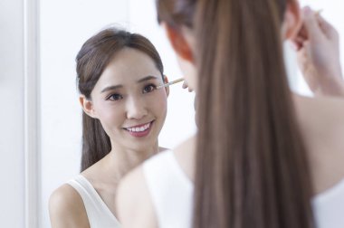 Ayna ve koyarak gülümseyen yüzü bakarak Genç Asyalı kadın makyaj