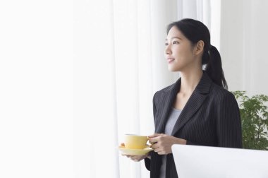 Bir fincan kahve tutarak ve uzağa arıyorsunuz gülümseyen Genç Asyalı kadın