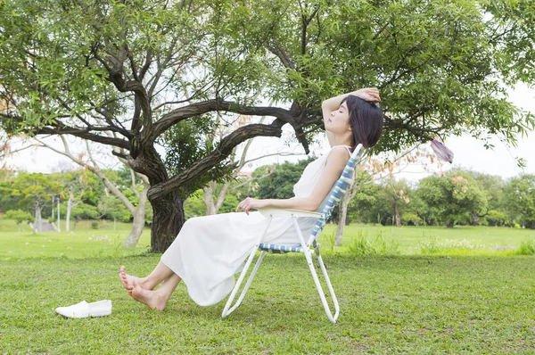 年轻的亚洲妇女穿着白色礼服坐在长凳上晒黑 — 图库照片