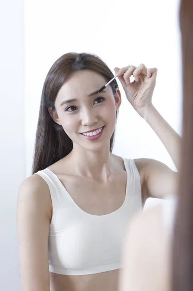 Young Asian woman looking at the mirror and smiling putting make up  onto her face