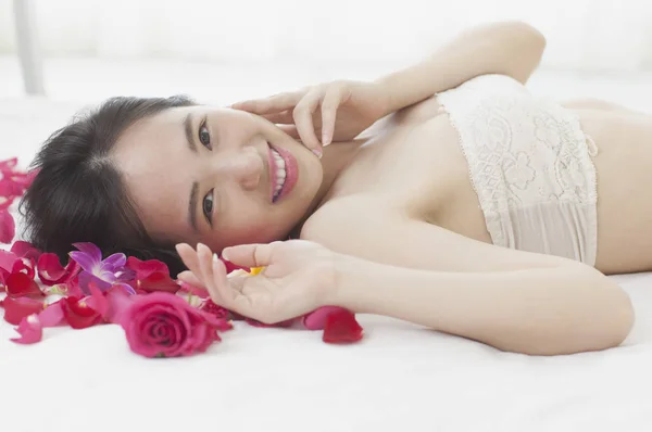 年轻的亚洲女人躺在玫瑰和微笑着对着镜头 — 图库照片
