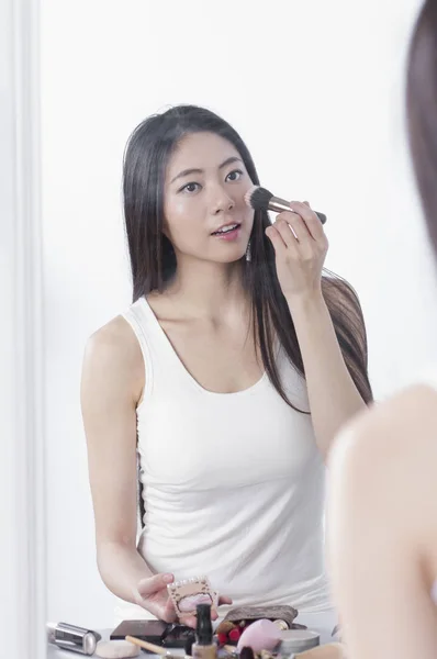 A beautiful Asian woman looking at the mirror and putting on makeup