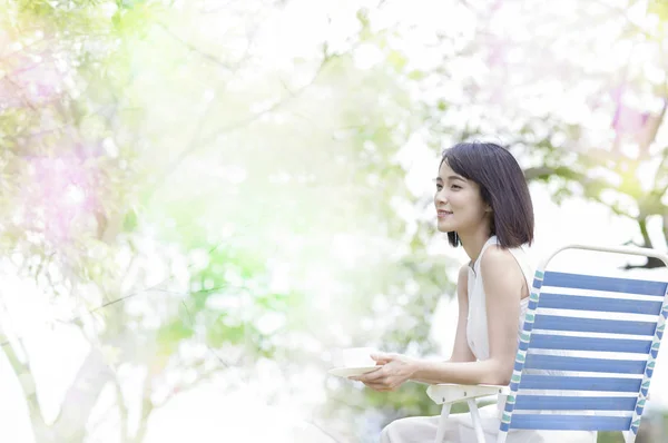 穿着白色礼服的年轻亚洲妇女坐在长凳上喝咖啡 — 图库照片