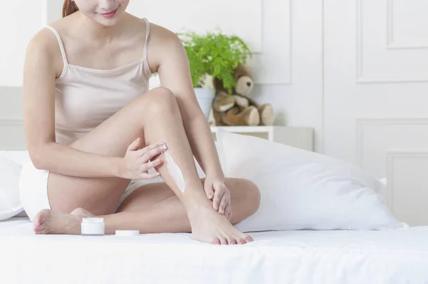 Young Asian woman putting lotion on her leg