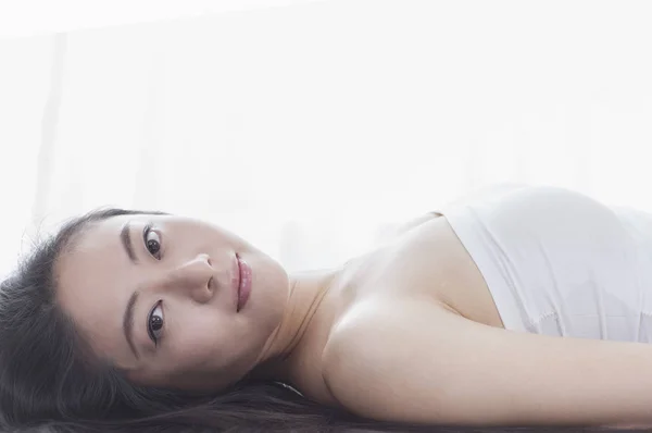 横になっている カメラで笑顔の長い黒髪の若いアジア女性 — ストック写真