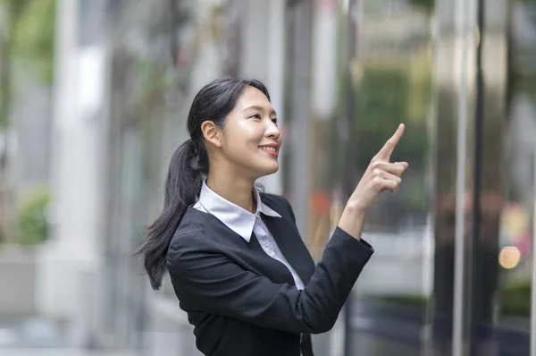 Young Asian woman wearing a suit hands up and pointing