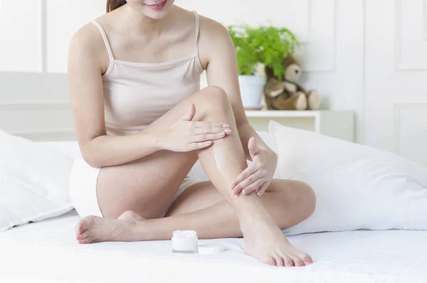 Young Asian woman putting lotion on her leg