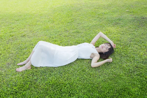 昼寝をして草の上に横になっている白いドレスを着ている若いアジア女性 — ストック写真