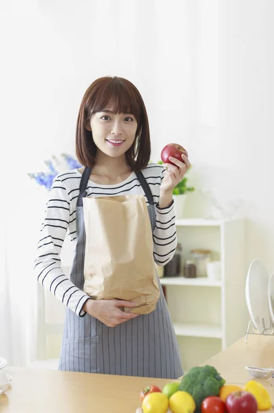 年轻的亚洲妇女拿着一个袋子和一个苹果对着镜头微笑 — 图库照片