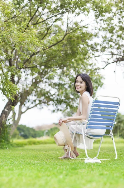 年轻的亚洲女人穿着白色的衣服坐在长凳上 对着镜头微笑 — 图库照片