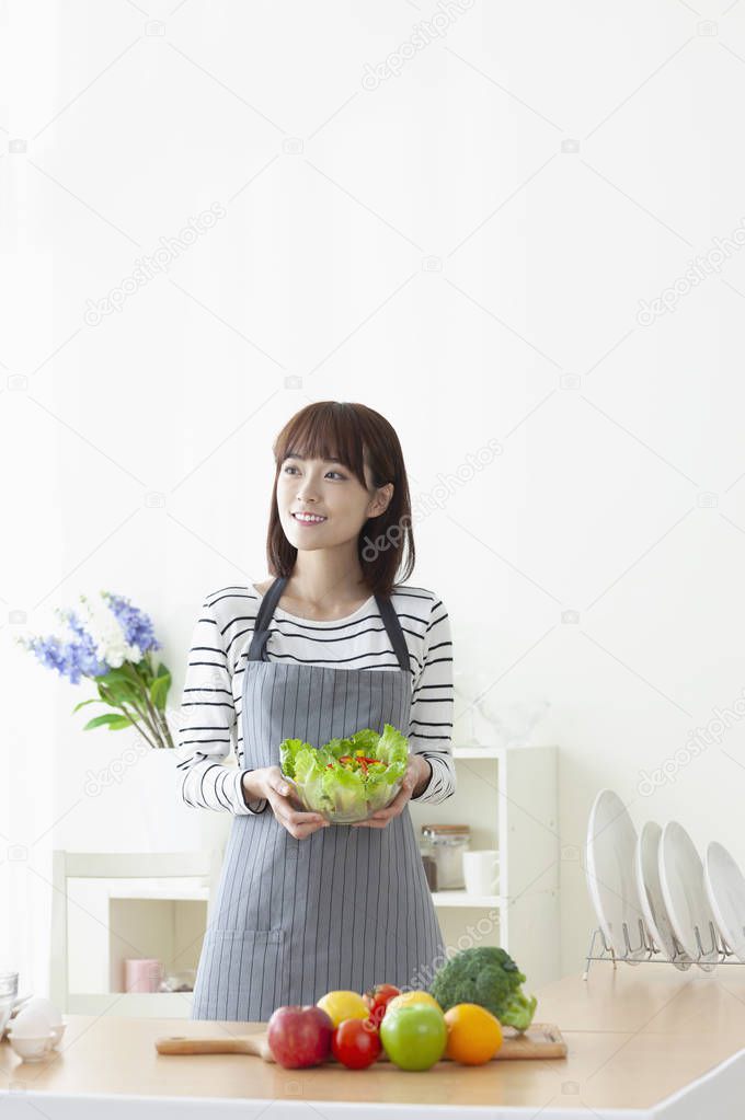 Young Asian woman holding up a bowl and salad and smiling
