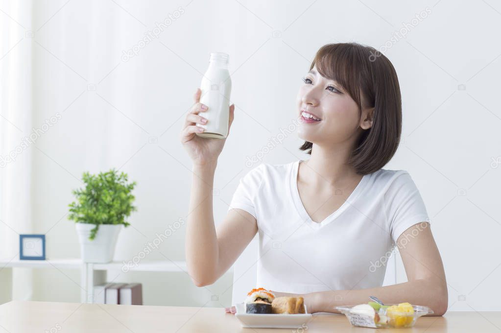 Young Asian woman holding a glass of milk and smiling looking at it