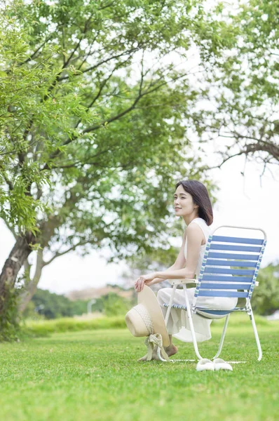 年轻的亚洲女人穿着白色的衣服坐在长凳上 微笑着望着看着离开 — 图库照片