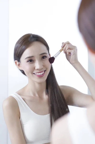 Young Asian woman looking at the mirror and smiling putting make up  onto her face