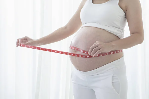一个孕妇的肚皮与测量磁带的背景 — 图库照片