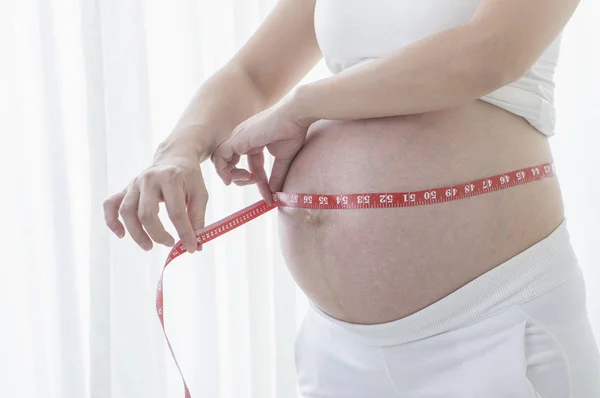 一个孕妇的肚皮与测量磁带的背景 — 图库照片