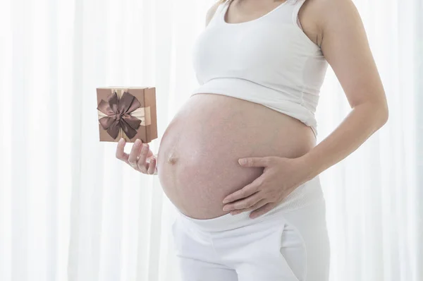 背景に贈り物を持つ妊娠中の女性の腹 — ストック写真