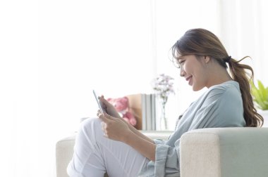 Güzel Asyalı kadın evde dijital tablet kullanıyor.