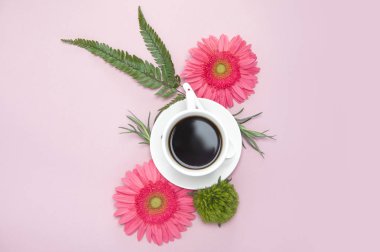Pembe arka planda bir fincan kahve ve çiçekler
