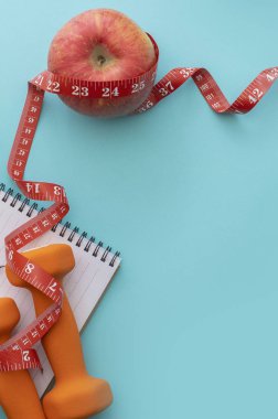 Kırmızı elma, not defteri, ağırlıklar ve mavi arka plandaki mezura..