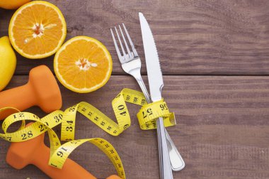 Meyveler, turunçgiller, ağırlıklar, çatal bıçak takımı ve tahta arka planda mezura..