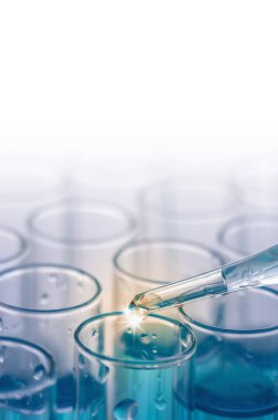 Beyaz zemin üzerinde sıvı ve pipetle laboratuvar camlarının yakın plan görüntüleri.