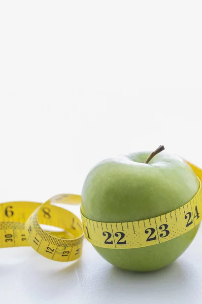 Beyaz arka planda yeşil elma ve mezura..