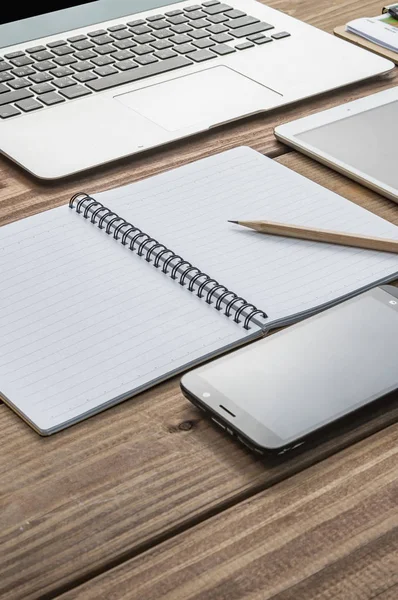 Ofis masasında kalem, dizüstü bilgisayar ve akıllı olan boş bir defter.