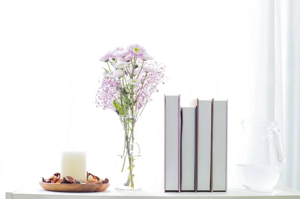 books, flowers in vase and candle with decor on a white background