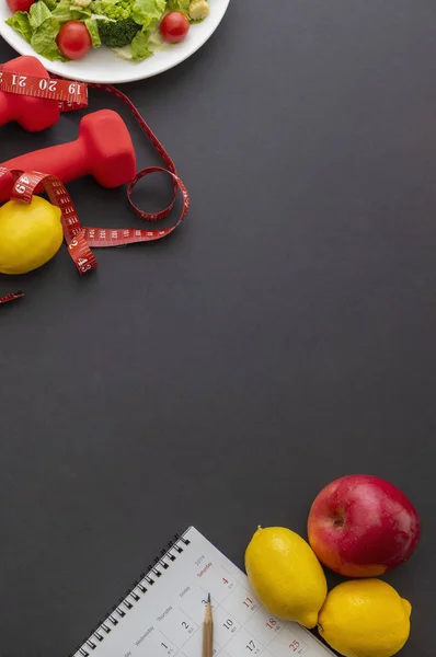 sağlıklı yaşam tarzı konsepti. Siyah zemin, mezura ve dambıl üzerindeki meyve ve sebzelerin üst görünümü 