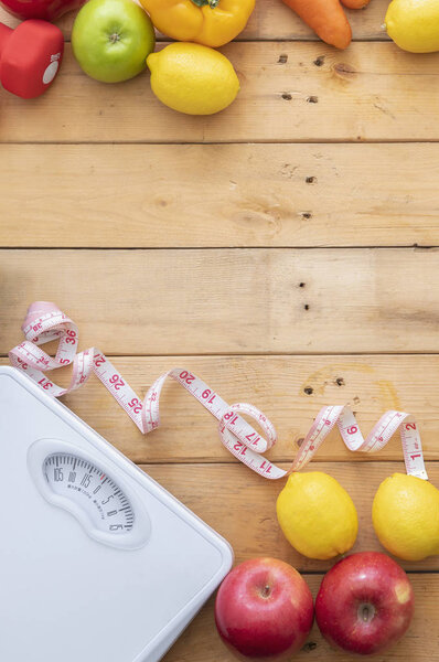 Фрукты, овощи, весы, весы и лента измерения на деревянном фоне.