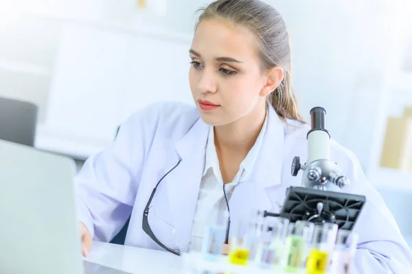 Young female scientist run an experiment or research in laboratory, with microscope and laptop. Medical healthcare technology, pharmaceutical research and development concept.