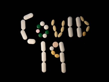 Siyah arka planda tıbbi tablet veya kapsül ile yazılmış COVID-19.