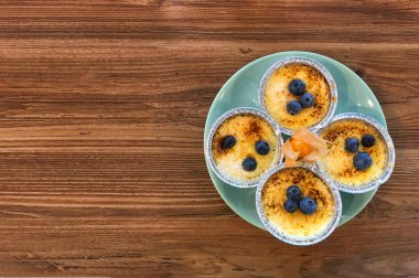 Turkuaz bir tabakta folyo kalıplı yaban mersinli puding ve ahşap bir masada turuncu fizsalis. Boşluğu kopyala