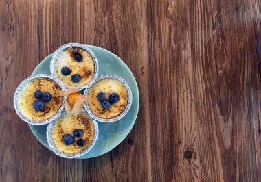 Turkuaz bir tabakta folyo kalıplı yaban mersinli puding ve ahşap bir masada turuncu fizsalis. Boşluğu kopyala