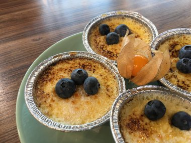 Turkuaz bir tabakta folyo kalıplı yaban mersinli puding ve ahşap bir masada portakal fizsalatası.. 